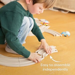 Child assembling a wooden track set on a floor with toy cars with the words 