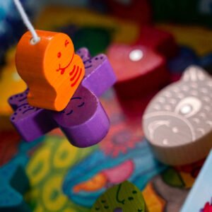 My Very First Games - Here, Fishy, Fishy! Magnetic Game's colorful wooden worm figurine hangs from a fishing line connected to a purple wooden octopus