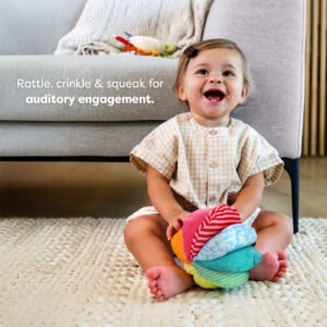 A young child sitting on a rug with a colorful toy ball, in front of a sofa with a blanket and toys. Text reads 'Rattle, crinkle & squeak for auditory engagement.