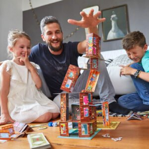 Dad with two laughing kids placing a Rhino Hero Super Battle card on top of a card tower as it falls down