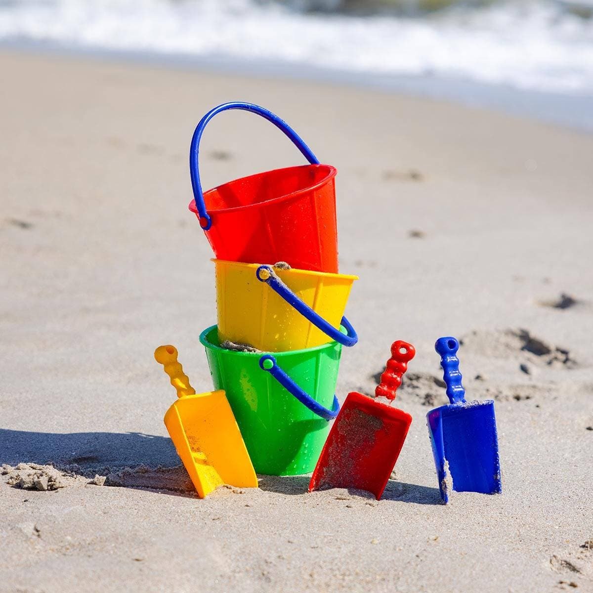 One red, yellow, and green pail on a beach with a red, yellow, and blue scoop
